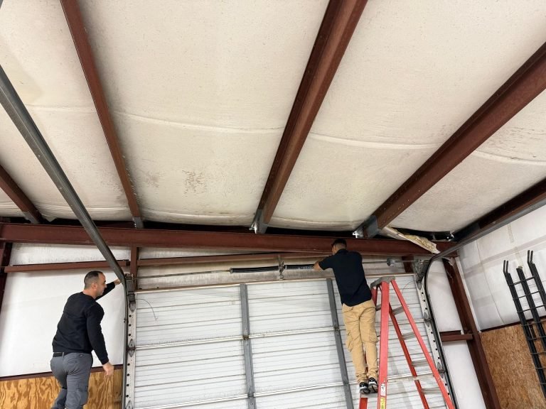 Two Garage Door Family technicians working on the shaft and track of a large commercial garage door
