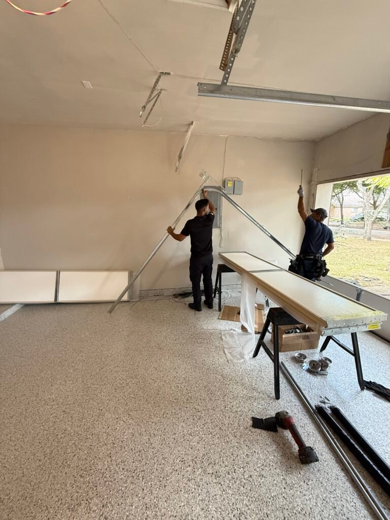 Two Garage Door Family technicians installing a new garage door with panels stacked on the driveway